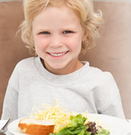 Niña sonriente, con un plato de ensalada. Foto alusiva al Día Mundial de la Alimentación